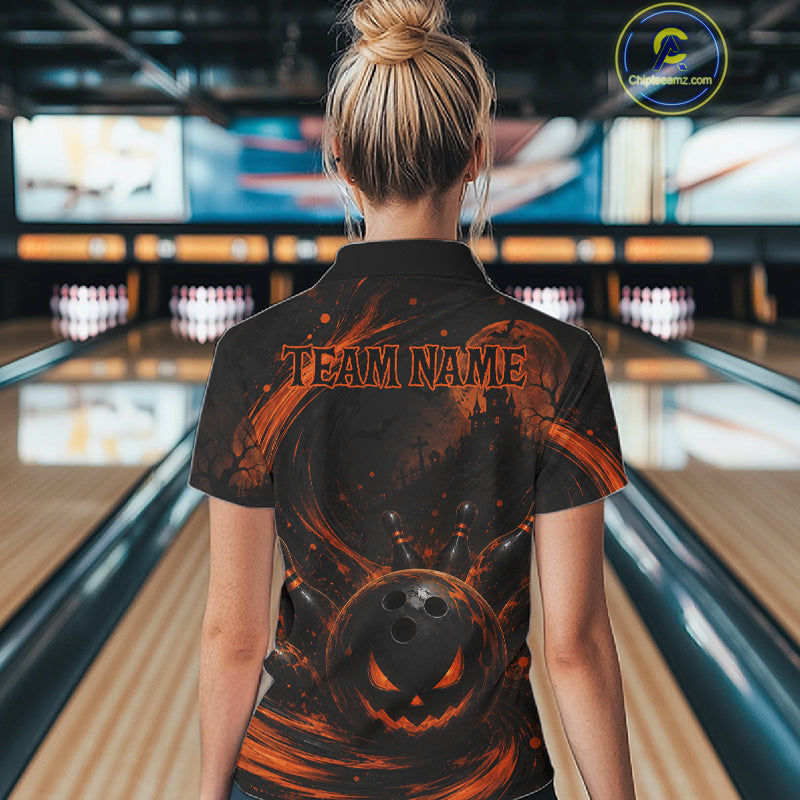 A woman viewed from behind wearing a black short-sleeve collared shirt with an orange Halloween-themed graphic print featuring a jack-o'-lantern, bowling pins, and the text 'TEAM NAME'. The background shows a blurred bowling alley interior.