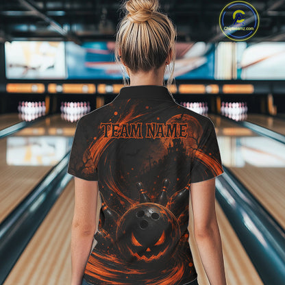 A woman viewed from behind wearing a black short-sleeve collared shirt with an orange Halloween-themed graphic print featuring a jack-o'-lantern, bowling pins, and the text 'TEAM NAME'. The background shows a blurred bowling alley interior.