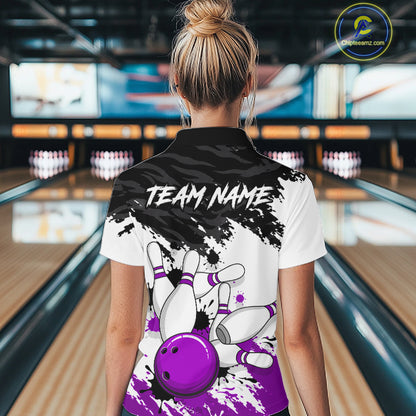 A woman viewed from behind wearing a customized bowling-themed polo shirt in a bowling alley. The back of the white and black polo shirt features a purple bowling ball and pins graphic, with 'TEAM NAME' printed in white text.