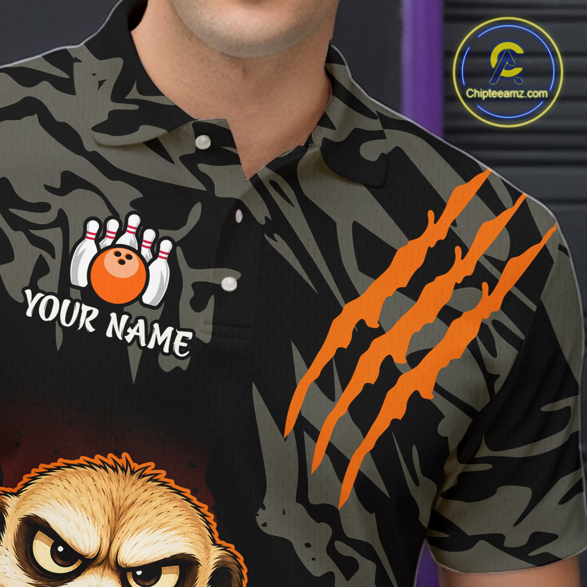 A close-up of a person wearing a short-sleeve polo shirt with a dark camouflage pattern, orange claw marks on the sleeve, a bowling pin graphic with a customizable 'YOUR NAME' text patch on the chest, and a cartoon animal face graphic at the bottom. A circular 'Chipteeamz.