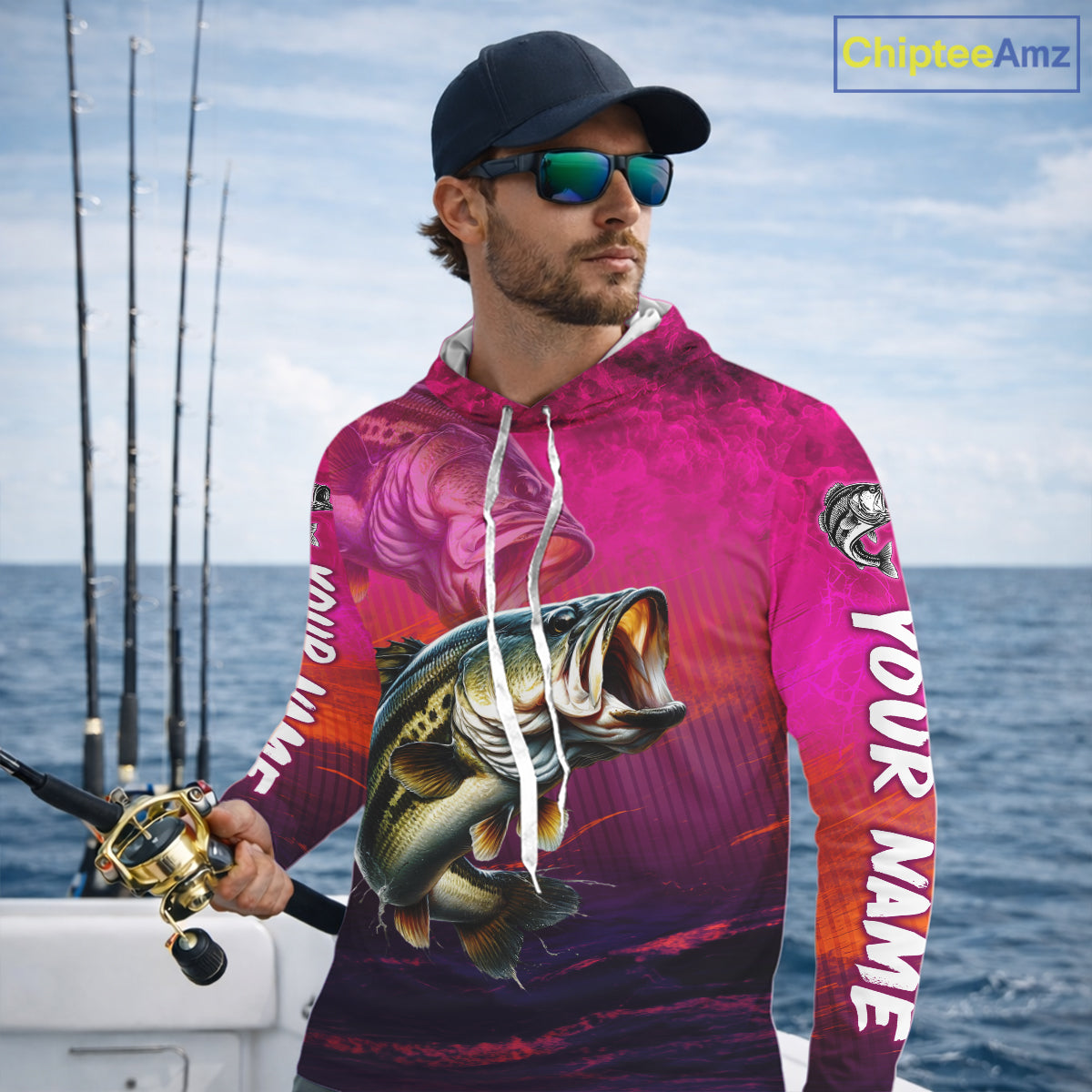 Man wearing a pink fishing-themed hoodie with a large fish graphic, standing on a boat with ocean and sky in the background.