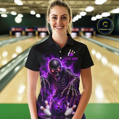 A woman stands in a bowling alley wearing a black short-sleeve polo shirt with a large purple and black horror graphic on the front, featuring a skull-like figure, bowling pins, and the text 'YOUR NAME' 