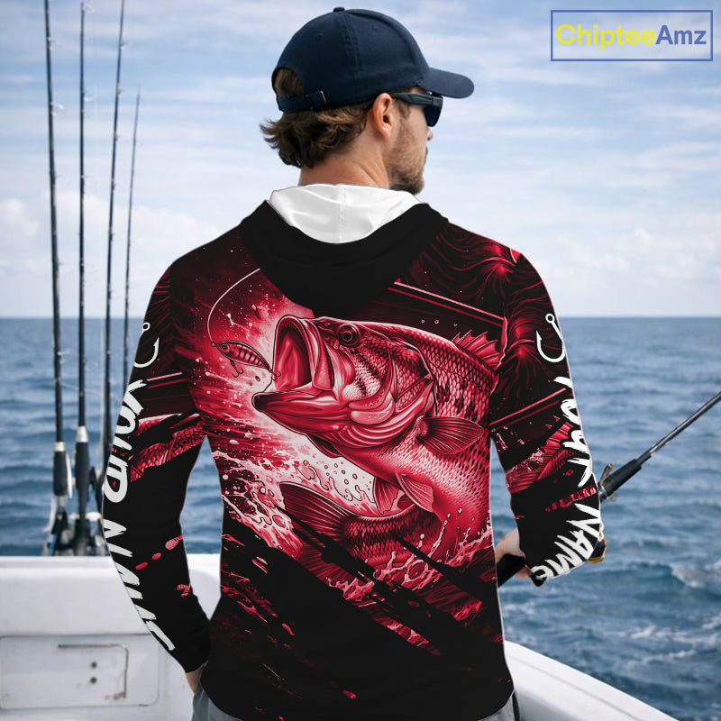 Person wearing a red and black bass hooded fishing shirt with a fish design, standing by the ocean.