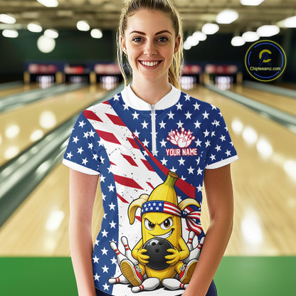 Woman wearing a patriotic-themed quarter zip shirt with a banana cartoon character holding a bowling ball in a bowling alley.