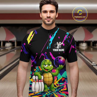 Man wearing a colorful bowling shirt with a turtle graphic in a bowling alley.