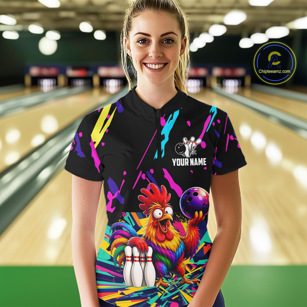 Person wearing a black bowling shirt with colorful design and chicken graphic in a bowling alley.