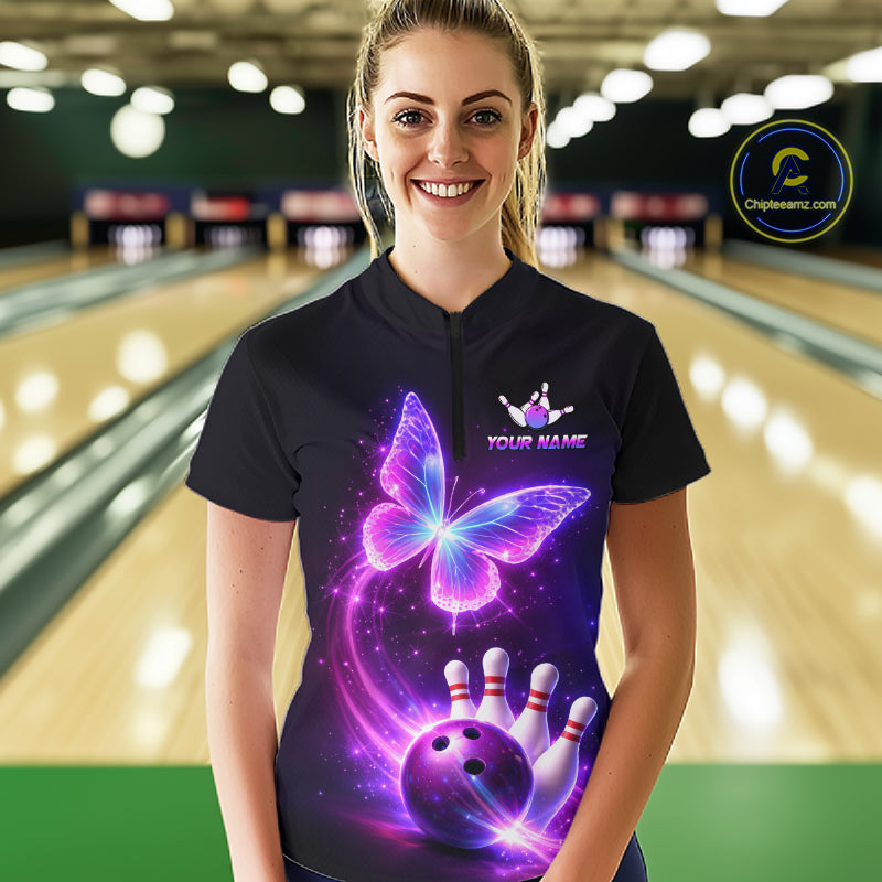 Person wearing a black bowling shirt with a butterfly and bowling ball design, standing in a bowling alley.